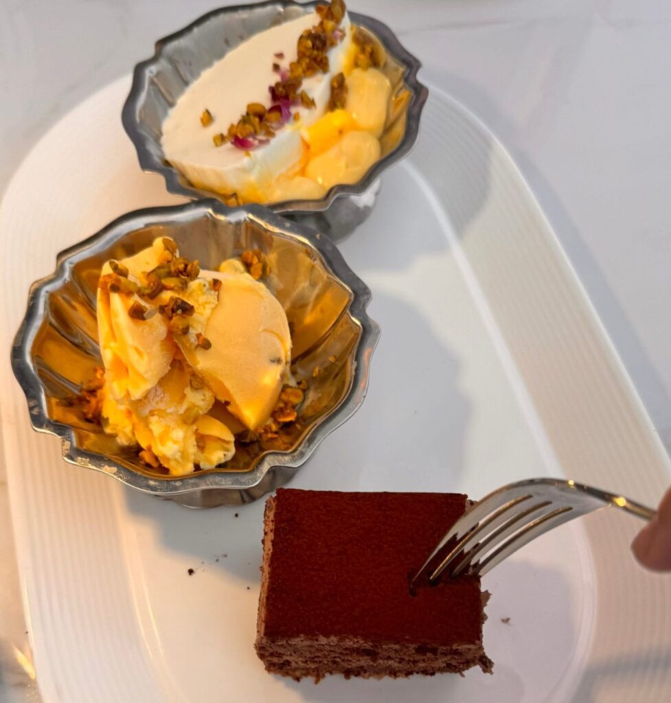 A Persian dessert platter featuring saffron ice cream with pistachios, saffron delight, and a square of Bibi chocolate cake being sampled with a fork at Perse in Brentwood.