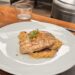 A grilled swordfish fillet with visible char marks served over a bed of savory orzo pasta, topped with crushed nuts and a sprig of fresh parsley at Fia Santa Monica.