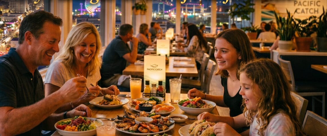 The Graham family (Ginger, Brad, Charlotte, and Madeline) smiling and enjoying a sensory diverse seafood spread at Pacific Catch restaurant, featuring a nighttime Santa Monica city in the background.