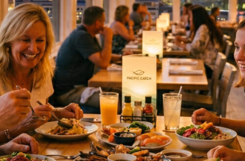 The Graham family (Ginger, Brad, Charlotte, and Madeline) smiling and enjoying a sensory diverse seafood spread at Pacific Catch restaurant, featuring a nighttime Santa Monica city in the background.