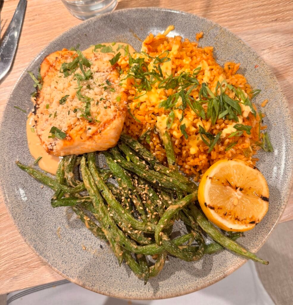A top-down view of a macadamia crusted salmon entree, sesame green beans, and kimchi fried rice on a grey plate at Pacific Catch Santa Monica.