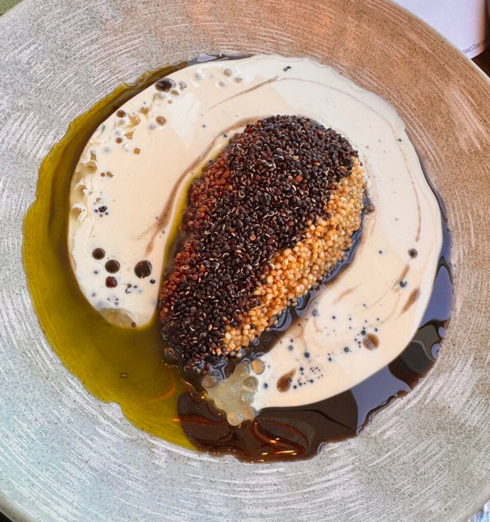 A gourmet Aguacate Relleno dish at Sendero, featuring a halved avocado coated in toasted quinoa, served in a pool of creamy white sauce and dark herb oil.