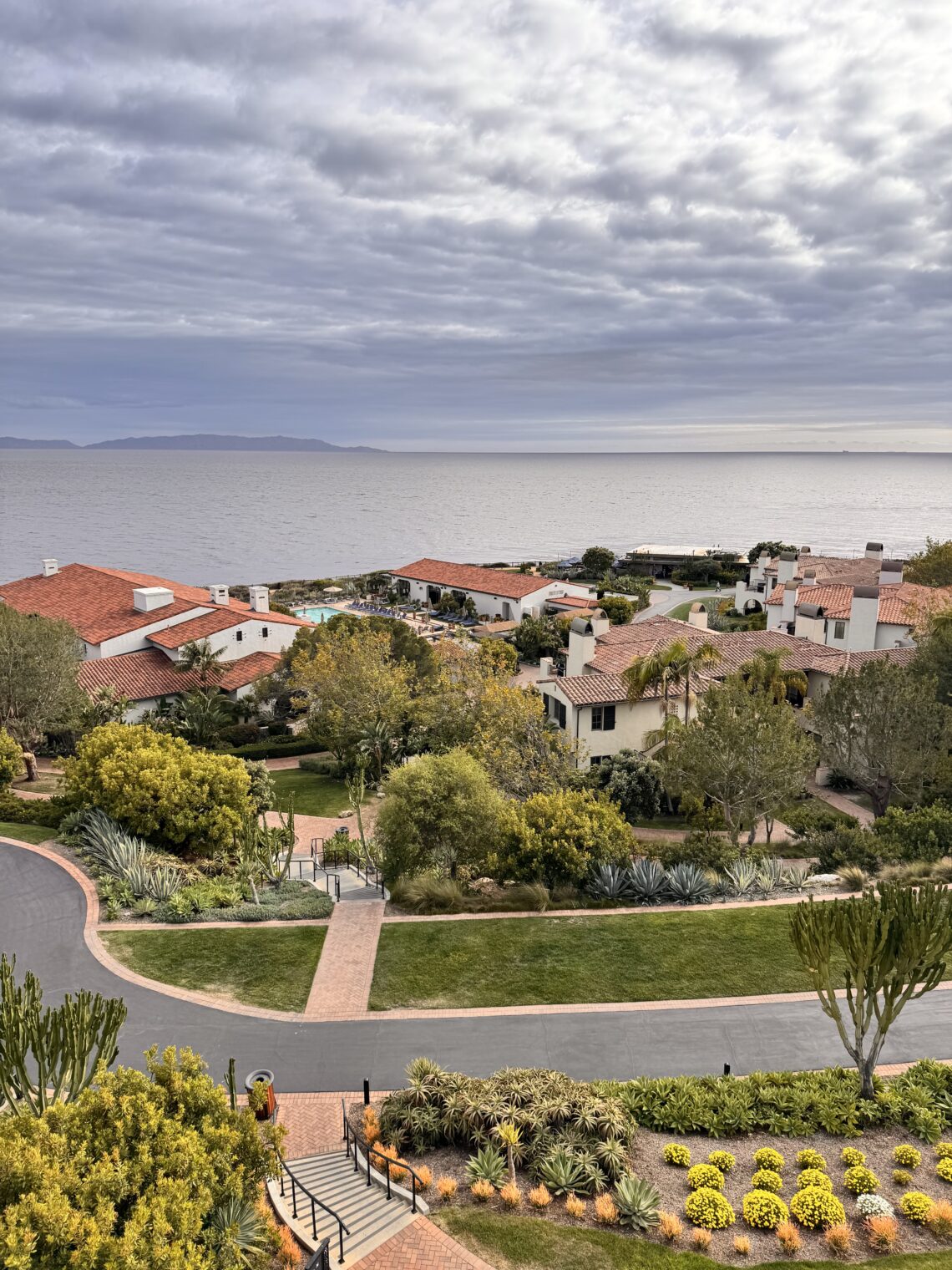 High-angle view of Terranea coastal resort with white buildings and red-tile roofs overlooking the ocean under a cloudy sky.