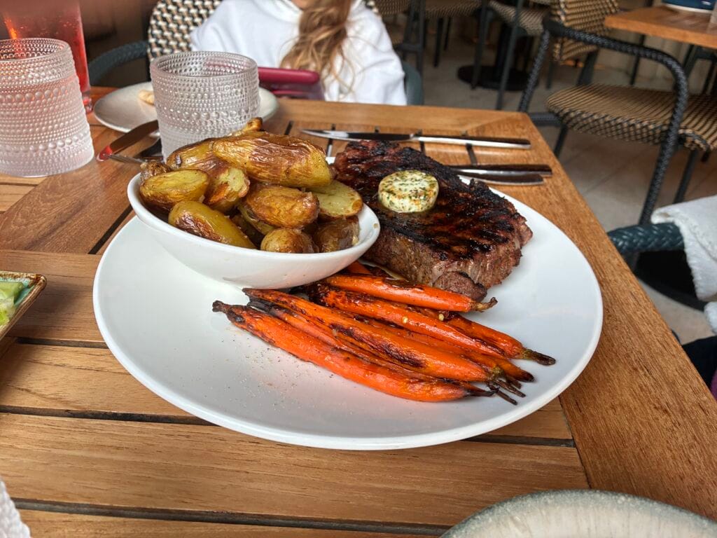 Coffee spice rubbed 14 oz prime ribeye with honey-glazed heirloom carrots, roasted fingerling potatoes, and garlic herb butter at Shoreside Restaurant and Bar in Santa Monica