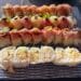 An overhead view of a large platter featuring four varieties of specialty sushi rolls, including the Tokubetsu Roll topped with delicate microgreens and black accents, the White Lotus Roll, a spicy tuna roll with jalapeño slices, and a popcorn shrimp tempura roll, served on a textured blue and white glass plate at Sushi Roku in Santa Monica.