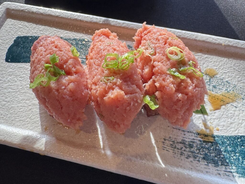 Close-up of three pieces of spicy tuna on crispy rice garnished with chopped green onions, served on a textured white and blue ceramic plate at Sushi Roku in Santa Monica.