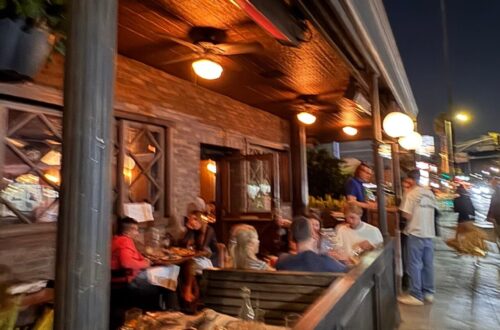 Exterior of Black Market Liquor Bar in Studio City at night with outdoor patio seating and guests dining