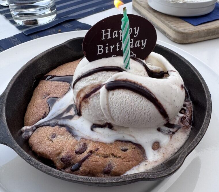 Deep dish chocolate chip cookie baked in a cast iron skillet, topped with vanilla bean gelato, chocolate sauce, a lit birthday candle, and a chocolate "Happy Birthday" plaque at Carbon Beach Club Restaurant at the Malibu Beach Inn