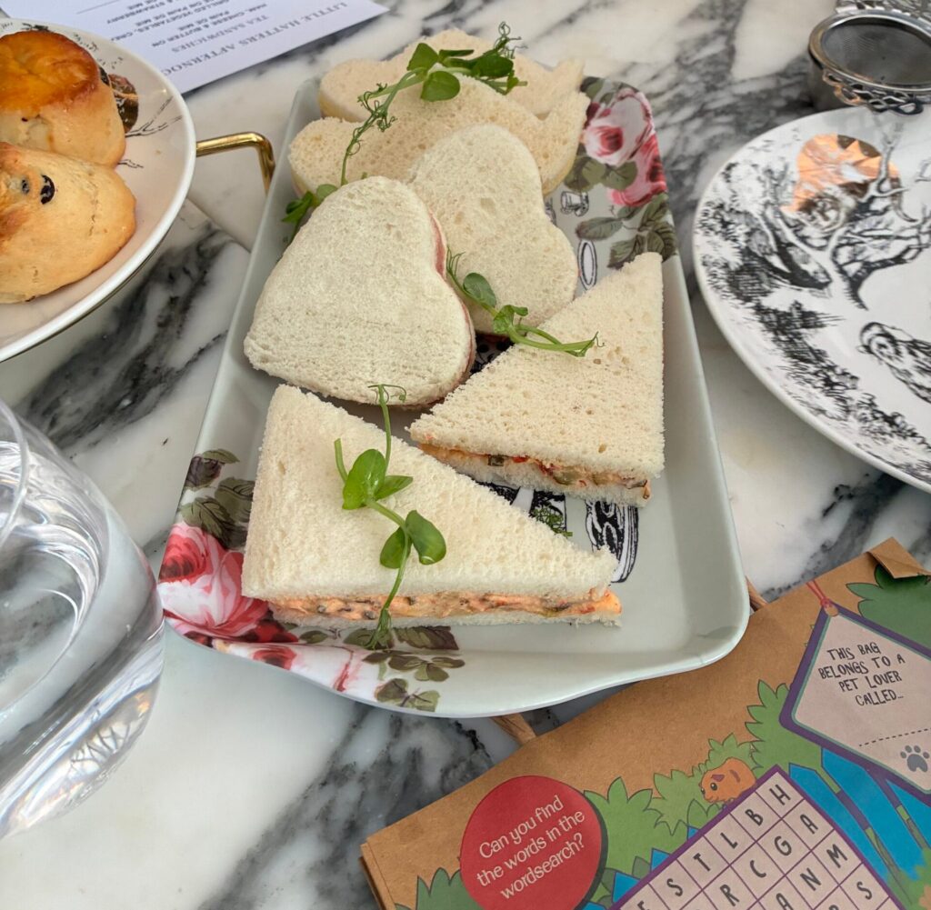 Kid’s tea sandwiches served at the Mad Hatters Afternoon Tea, arranged as heart and triangle shapes on a floral-patterned plate with fresh microgreens.