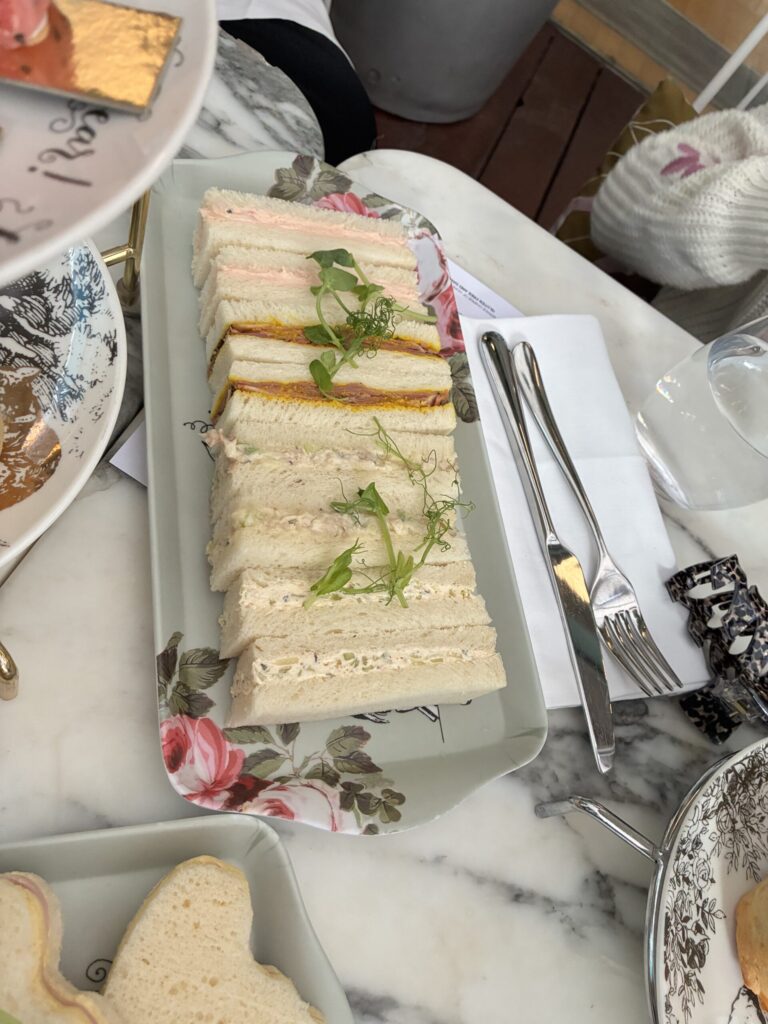 Adult tea sandwiches served at the Mad Hatters Afternoon Tea, arranged in neat rows on a floral-patterned plate and garnished with fresh microgreens.