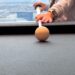 A child's hand lines up a shot on the pool table in our suite at the Venetian, with the Las Vegas skyline and mountains visible through the window