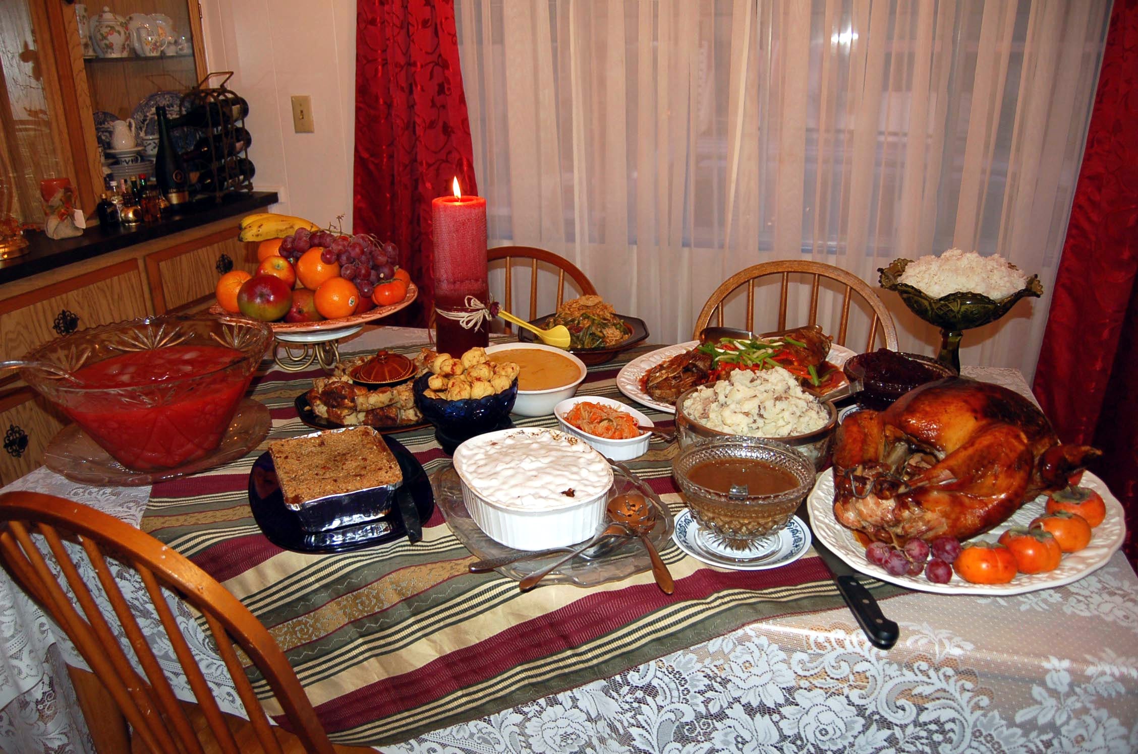 A Thanksgiving table set with a roasted turkey and an assortment of side dishes, pies, and drinks contributed by different guests