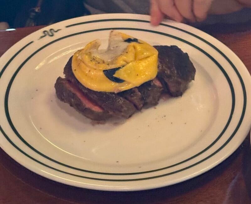 Sliced filet mignon topped with a large golden Cacio e Pepe Raviolo on a white plate at Bad Roman.