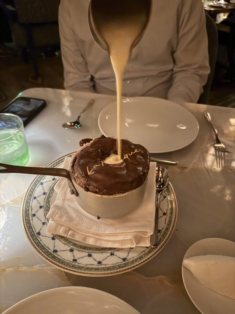 Vanilla sauce being poured into a chocolate soufflé at the table