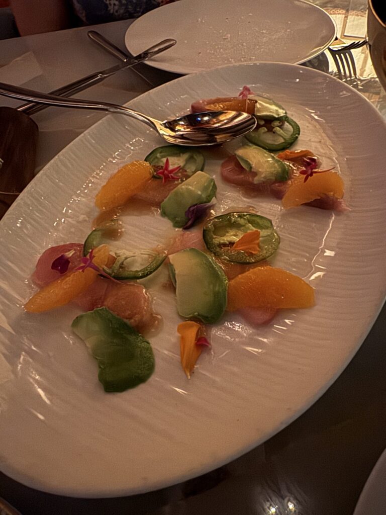 Hamachi crudo with orange segments, avocado, sliced jalapeño, and edible flowers