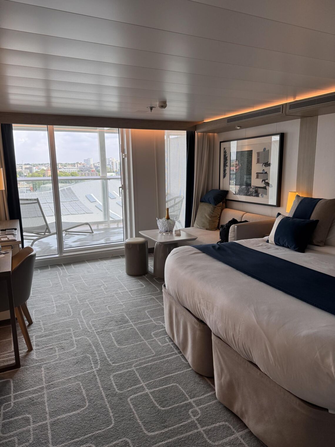 The Celebrity Edge-class Sky Suite bedroom with a plush bed and floor-to-ceiling views out to the balcony and rooftop.