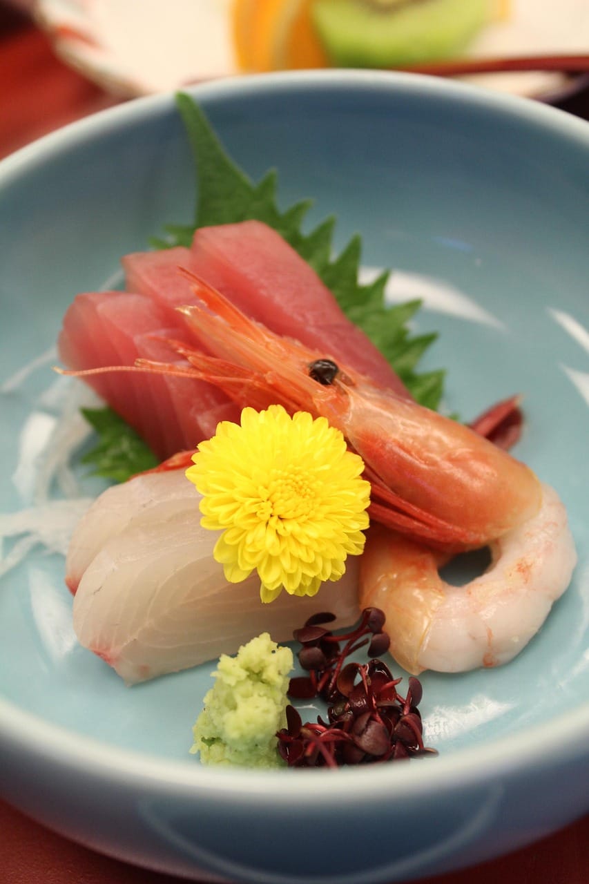 An elegantly plated seafood course with sashimi, shrimp, and a garnish of chrysanthemum petals, evoking the refined tasting-menu style served at Corridor 109 in Los Angeles