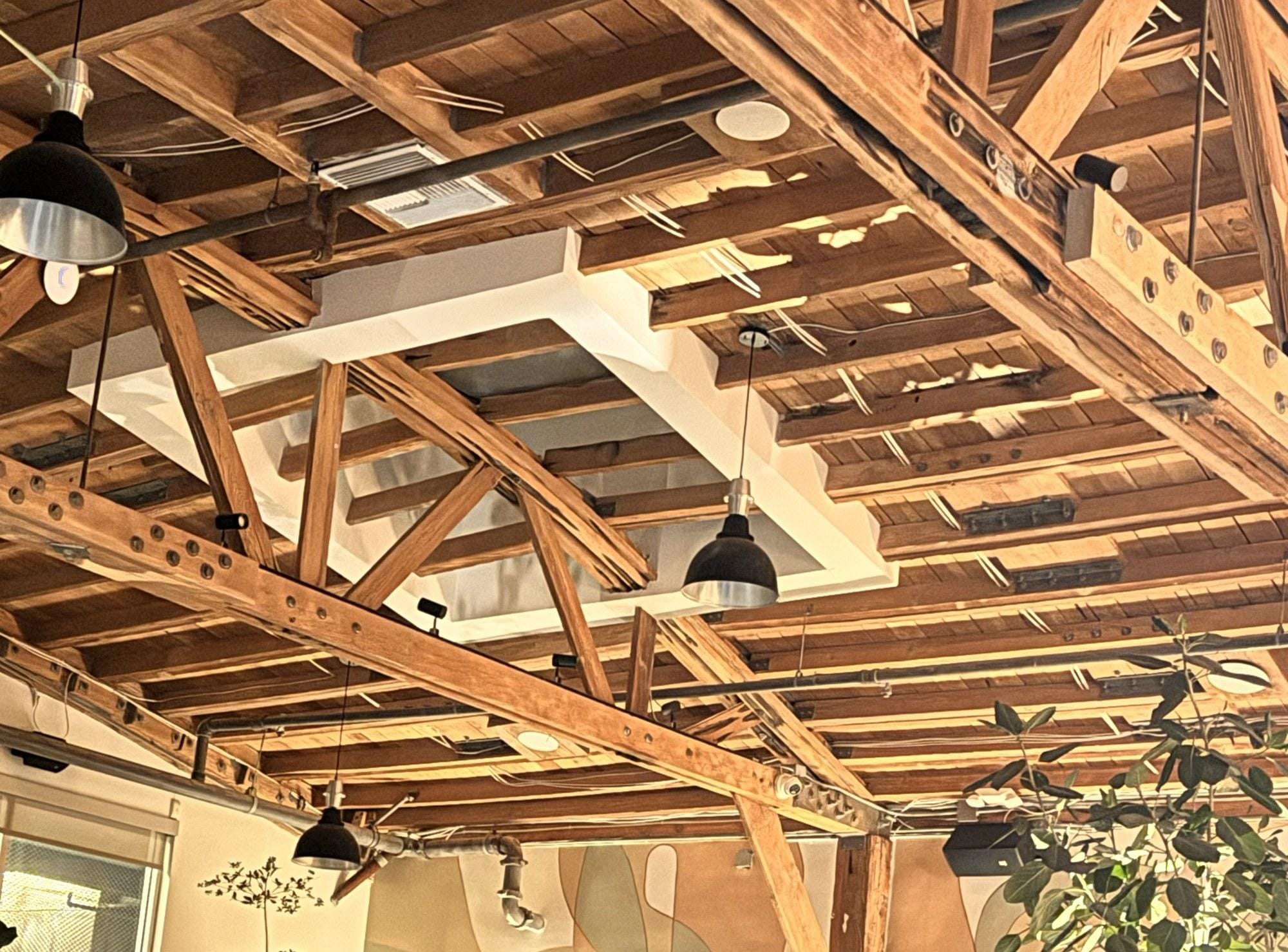 Exposed wood roof trusses and hanging pendant lights inside one of the Edgemar restaurants, showing the raw, unfinished materials Frank Gehry left visible throughout the complex.
