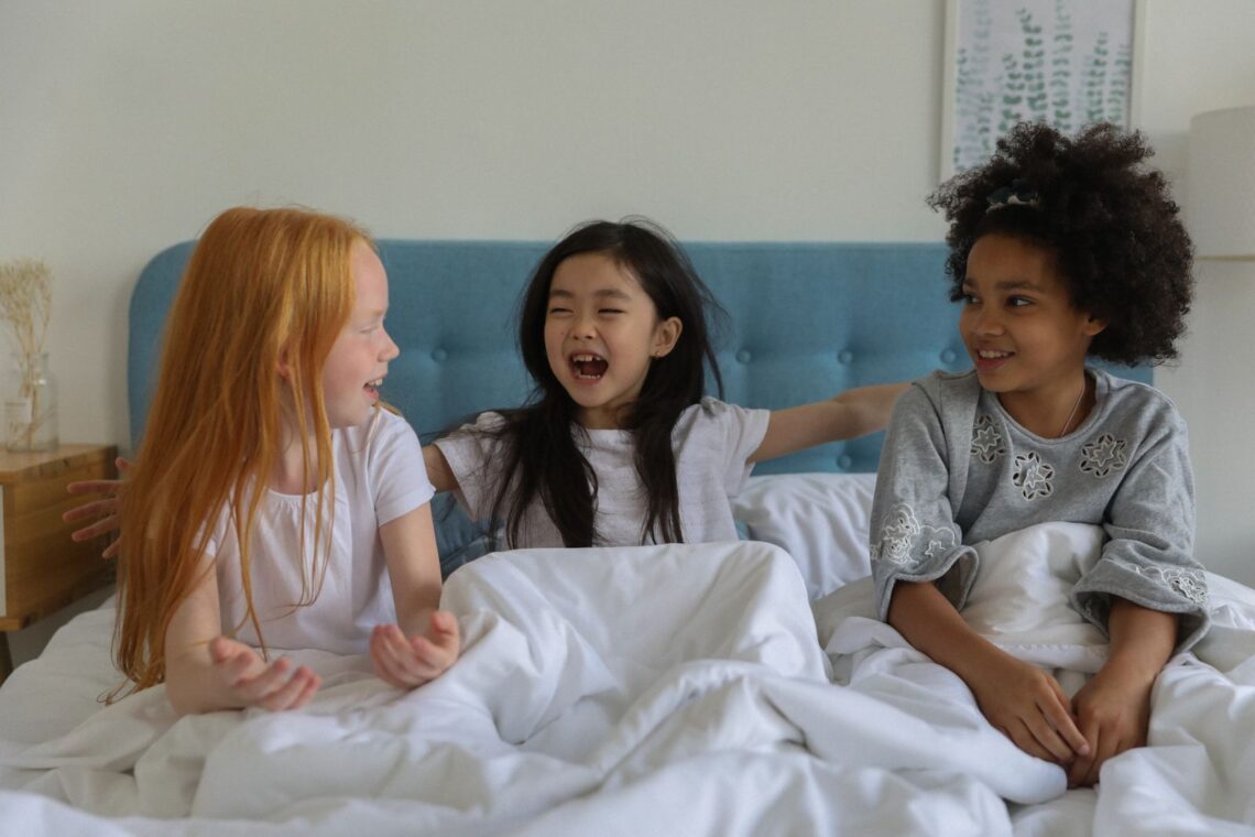 Three girls laughing together on a bed during a hotel sleepover birthday party, similar to the pajama-clad group at Charlotte's party