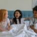 Three girls laughing together on a bed during a hotel sleepover birthday party, similar to the pajama-clad group at Charlotte's party