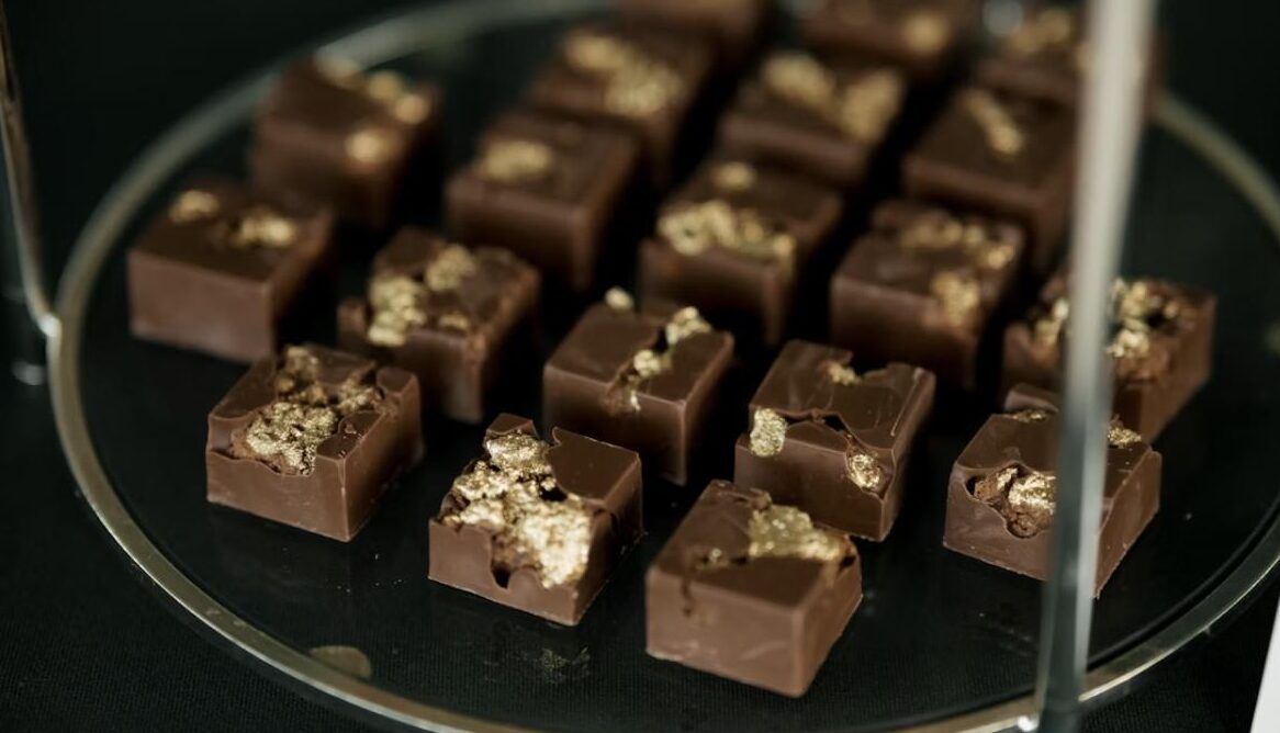 Dark chocolate bonbons topped with real edible gold leaf flakes, displayed on a glass tiered stand.