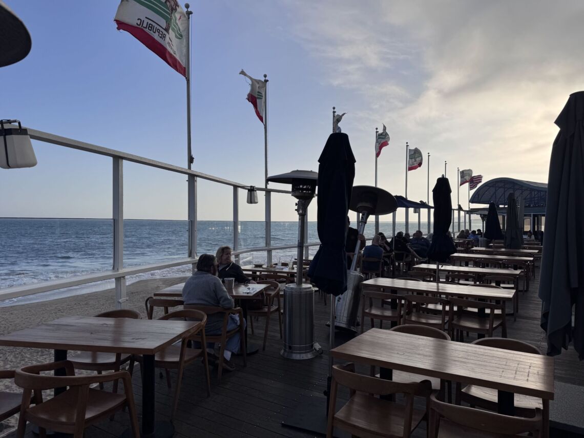 Outdoor oceanfront patio at Gladstones Malibu with wooden tables and California flags along the railing