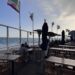 Outdoor oceanfront patio at Gladstones Malibu with wooden tables and California flags along the railing