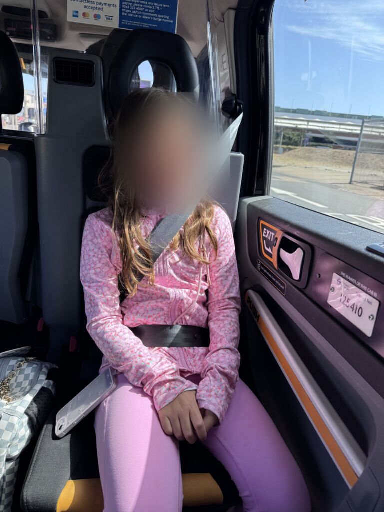 Girl sitting in the rear-facing fold-down seat of a London black cab, face blurred for privacy