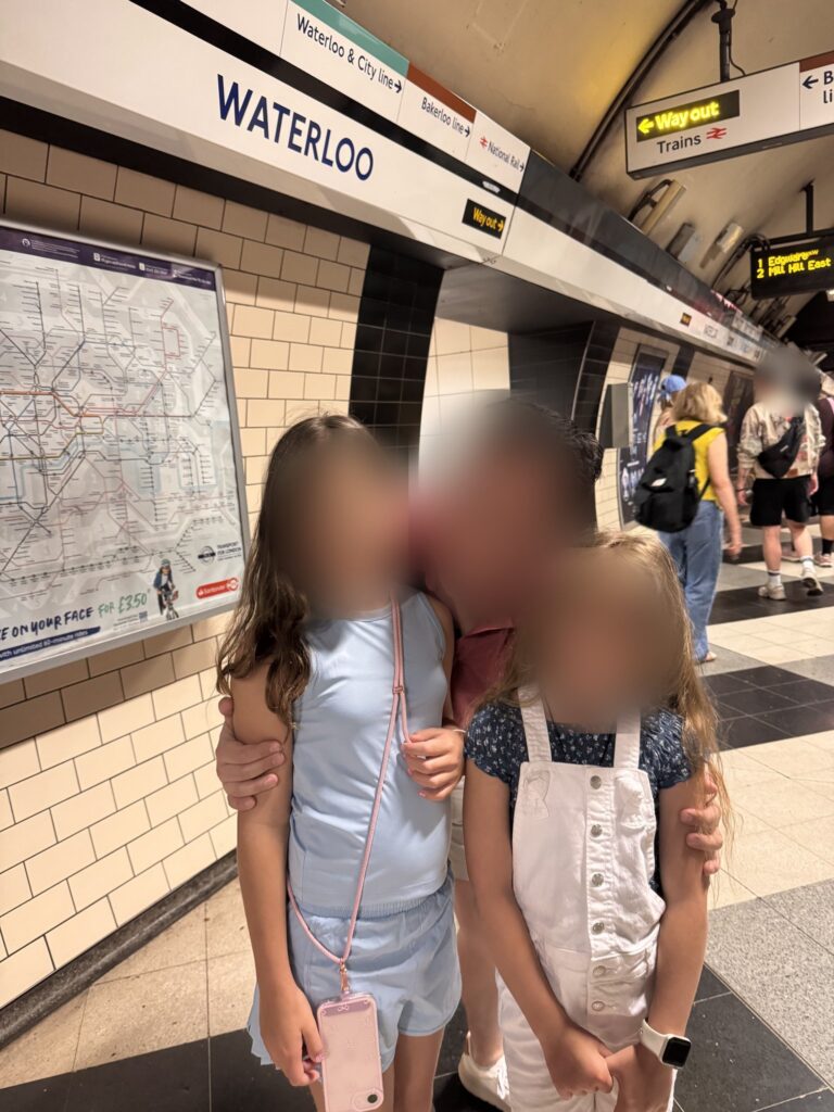 Father and two daughters on the Tube platform at Waterloo station in London, faces blurred for privacy