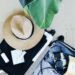 A packed suitcase for a luxury cruise with a straw sun hat, black separates, a rose facial mist, and a vintage camera, flat-lay style.