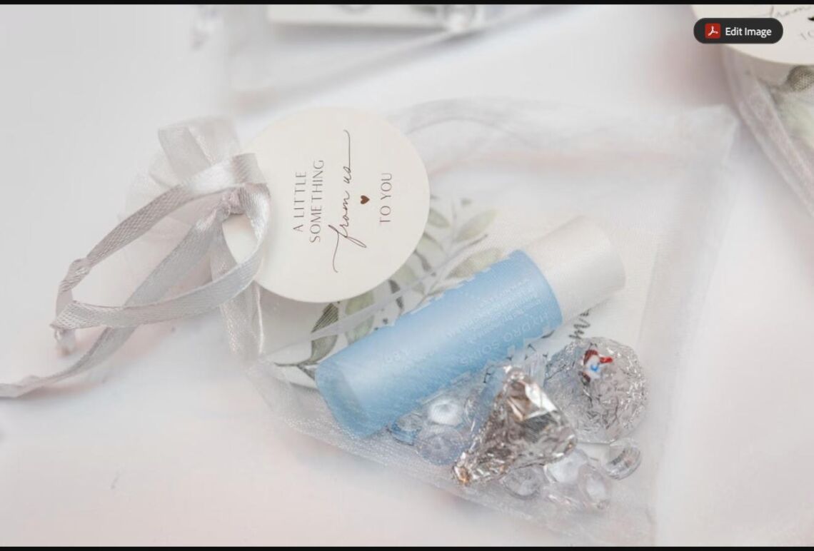 An elegant sheer organza favor bag tied with ribbon, filled with a small gift and wrapped chocolates on a white surface (stock photo, used for illustration)