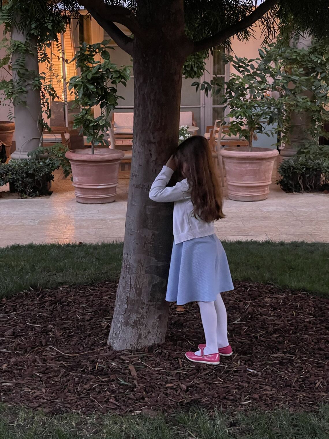 Madeline playing hide-and-seek by a tree in the courtyard at The Terrace at The Maybourne while we waited for dinner