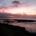 Pink and orange sunset over the North Shore coastline near Turtle Bay, Oahu, with dark lava rock in the foreground — the view near Alaia restaurant at dinner time.