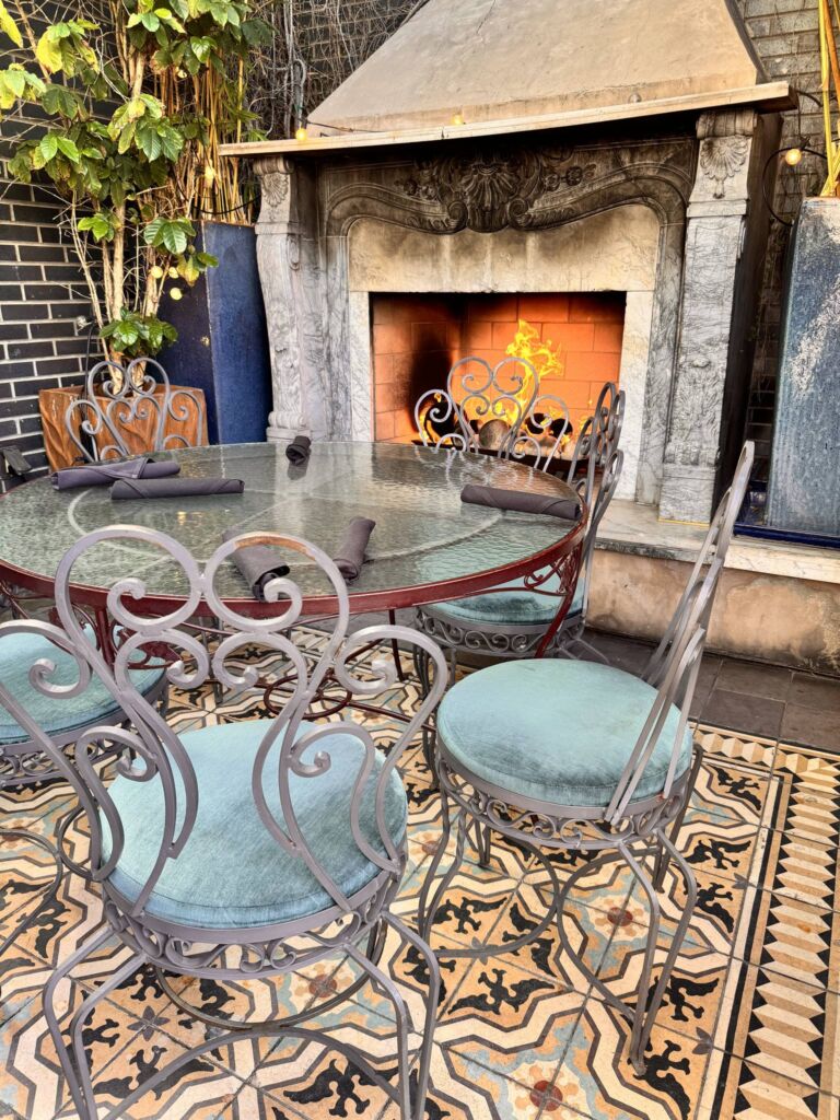 A wrought-iron dining table set for brunch on an outdoor terrace beside a lit stone fireplace at Perch LA.