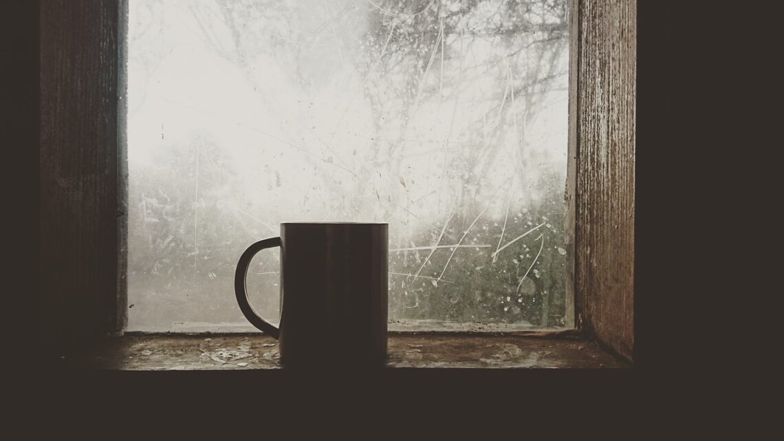 A dark mug sitting on a foggy, rain-streaked wooden windowsill looking out into misty forest, evoking a quiet Pacific Northwest lodge morning