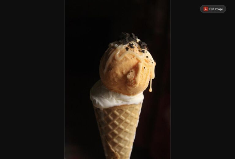 A double-scoop waffle cone with caramel drizzle and chocolate shavings (stock photo, used for illustration)