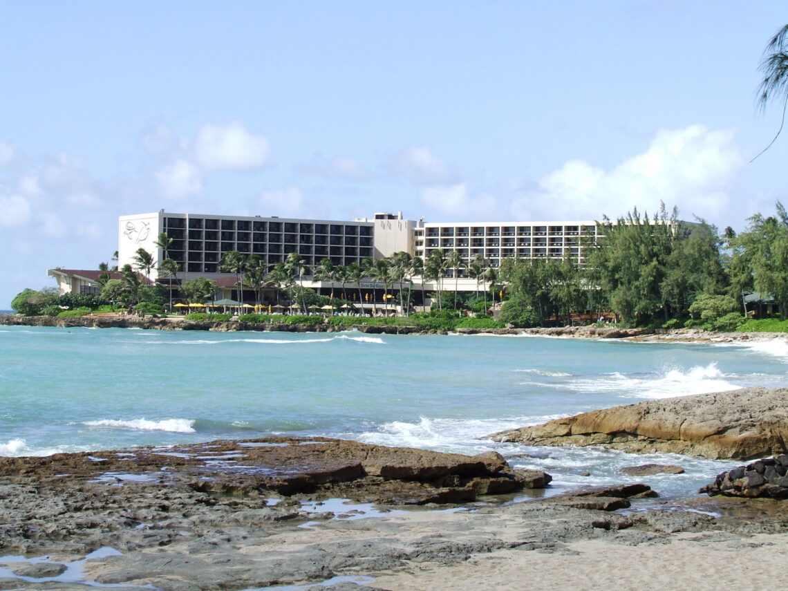 Turtle Bay Resort hotel building on its coastal point, with waves breaking on the rocky shoreline in the foreground