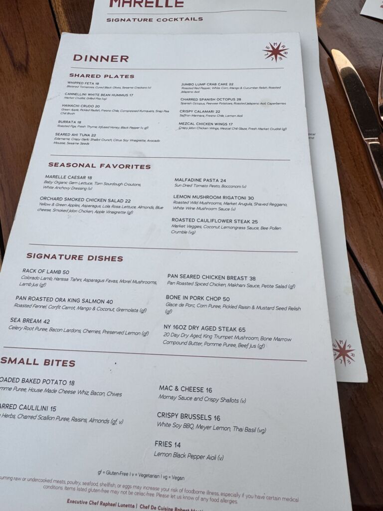 The Marelle dinner menu on a wooden table, listing small bites, seasonal favorites, and signature dishes