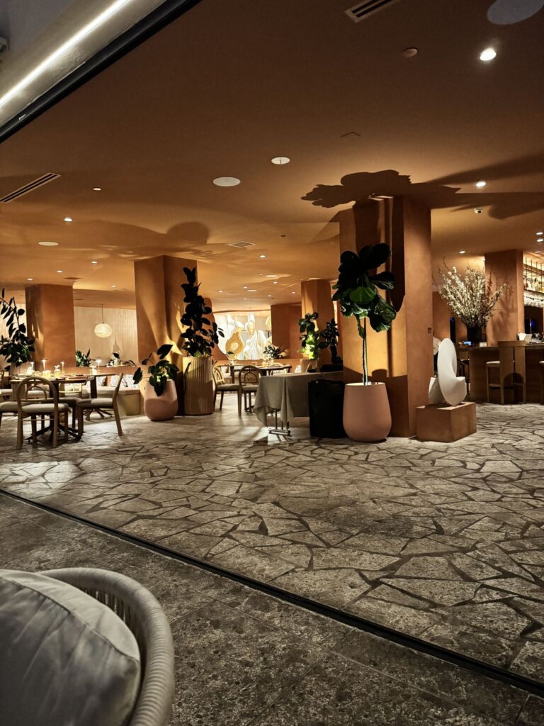 The softly lit dining room at Marelle in Santa Monica, with stone floors, terracotta columns, potted trees, and tables set for dinner