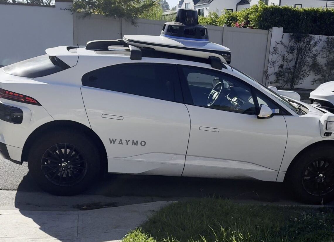 A white Waymo self-driving Jaguar with its roof sensor, parked on a residential street