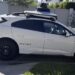 A white Waymo self-driving Jaguar with its roof sensor, parked on a residential street