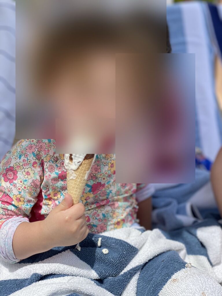 Child eating an ice cream cone on a beach towel