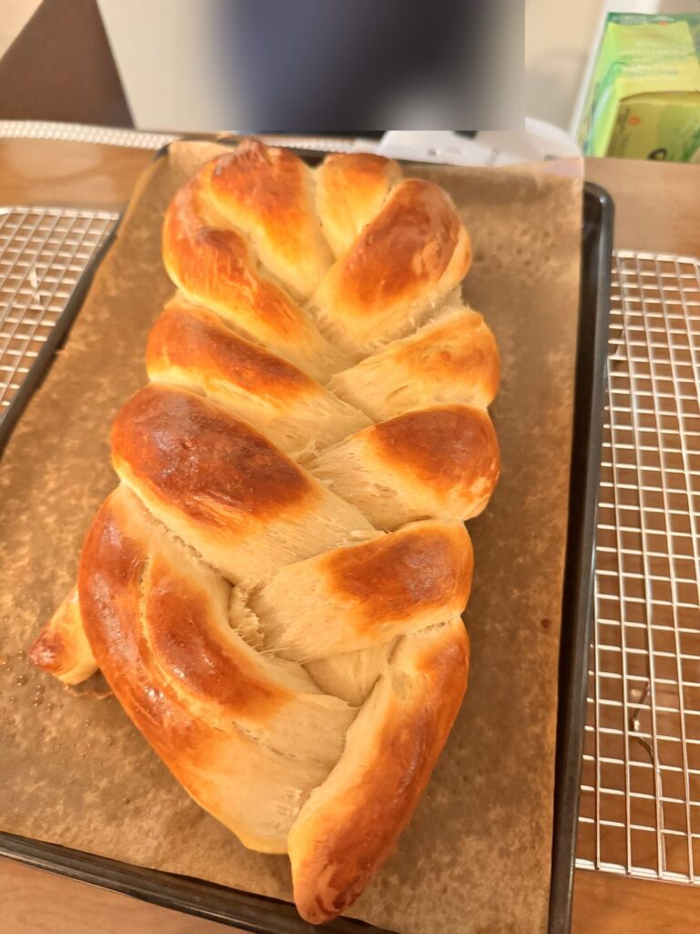 A golden braided challah cooling on a baking sheet