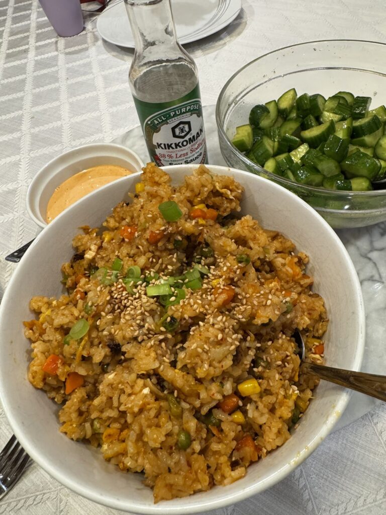 A big bowl of kimchi fried rice with a bowl of smashed cucumbers and spicy mayo
