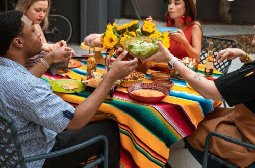 Friends passing bowls of food family-style across a colorful dinner table