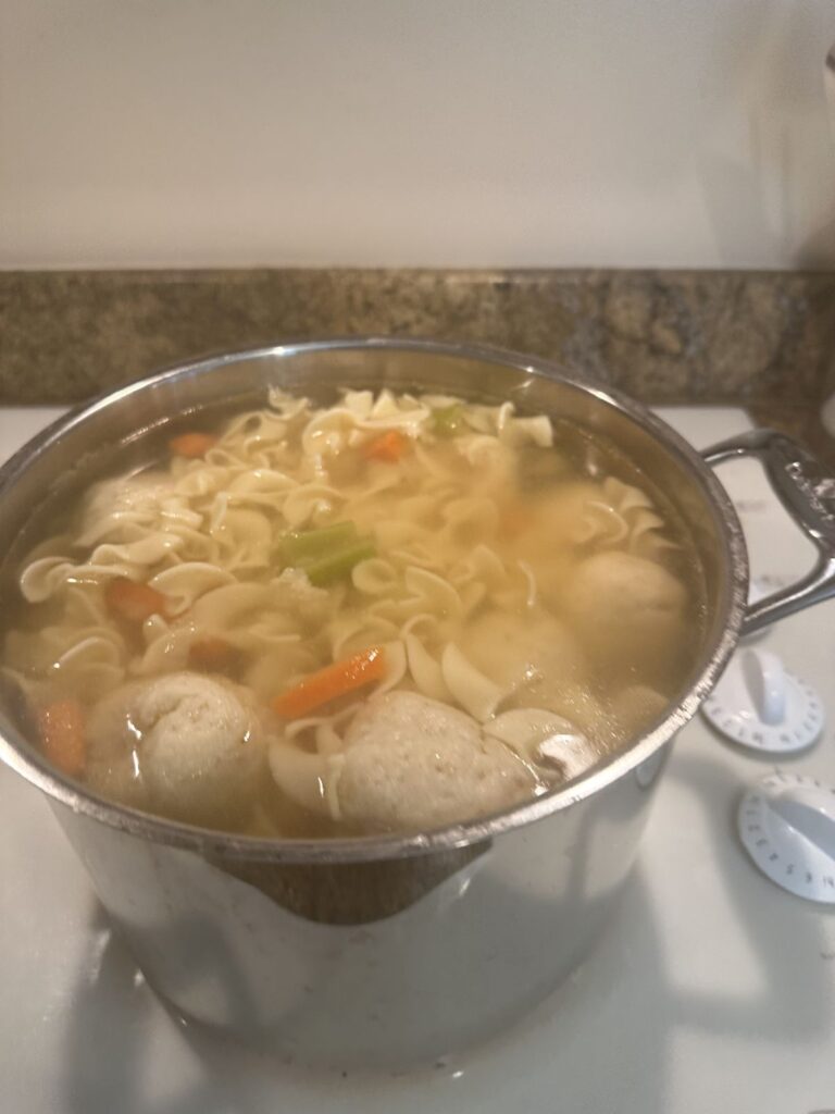 A pot of chicken noodle soup with matzo balls on the stove