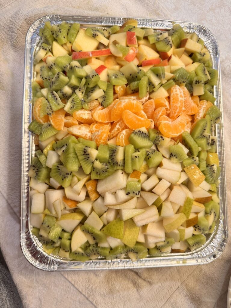 A tray of fruit salad with apples, pears, kiwi, and mandarin oranges