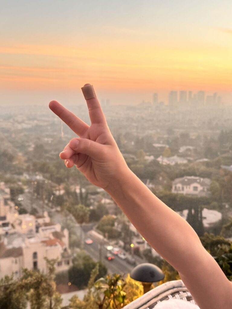 A child giving a peace sign over the Los Angeles skyline at sunset from The Roof