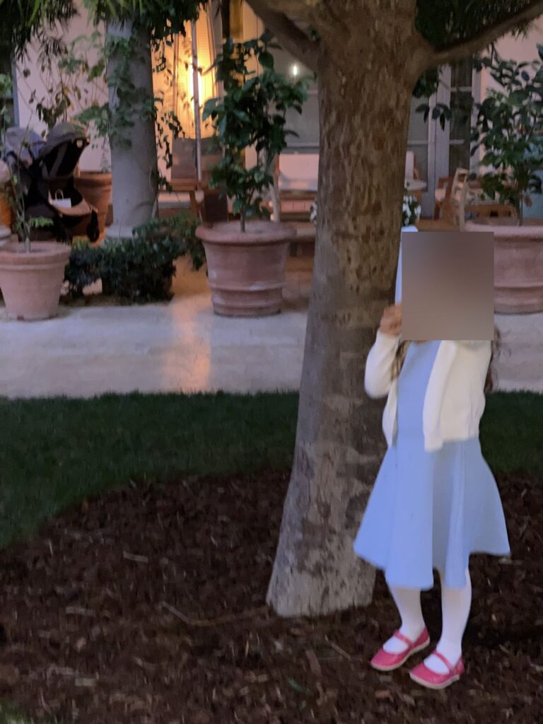 Our daughter playing by a tree in the garden near The Terrace at dusk, face blurred