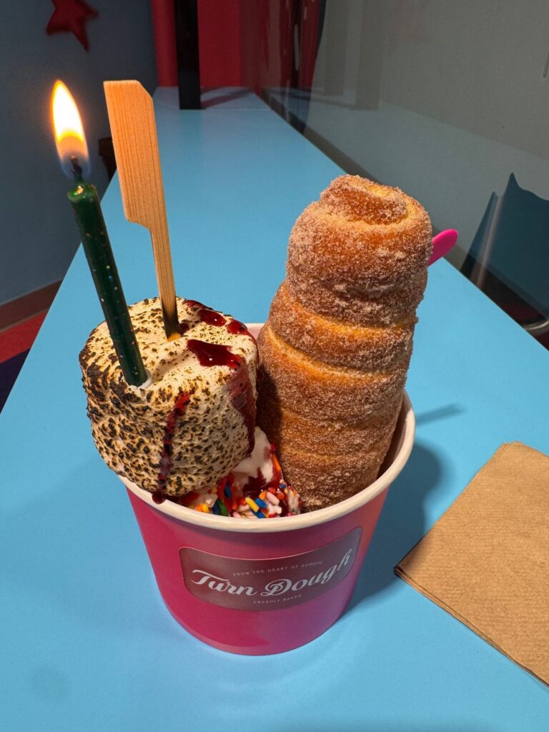 A Turn Dough chimney cake with soft-serve, sprinkles, and a toasted marshmallow in a pink cup, with a birthday candle